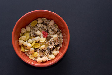 Close up muesli in ceramic red bowl isolated on black background. Heathy food, breakfast.
