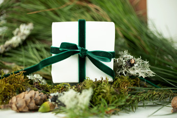White present wrapped with green velvet ribbon against fir branches.
