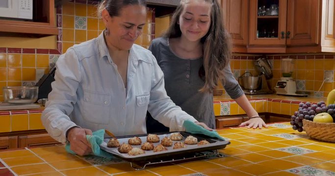 Proud mother removing cookies from the oven with her teenager daughter