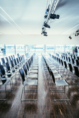 Lichtdurchfluteter Vortragsraum mit leeren Stühlen und Scheinwerfern an der Decke