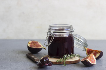 Fig jam or marmalade in a preserving glass or jar, figs and thyme on grey concrete background.