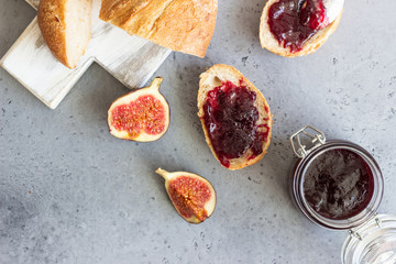 Sandwiches with fig jam. Chiabatta for sandwiches on a white wooden cutting board, figs and glass jar with jam on grey concrete background. Top view.