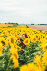Young beautiful woman in a dress among blooming sunflowers. Agroculture.