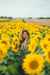 Fototapeta na wymiar Young beautiful woman in a dress among blooming sunflowers. Agroculture.