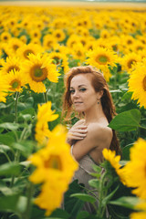 Young beautiful woman in a dress among blooming sunflowers. Agroculture.