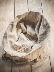 Burlap bag of white wholemeal flour on wooden rustic boards background.
