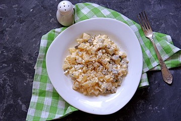 American potato salad with eggs and marinated cucumber on a dark gray background. Served with dressing from mayonnaise and mustard. Top view.