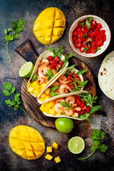 Mexican shrimp tacos with avocado, tomato, mango salsa on rustic stone table. Recipe for Cinco de Mayo party. Top view, overhead, flat lay.