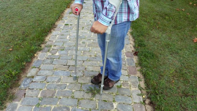 Man with crutches on a cobbled path