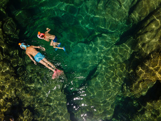 Snorkelling boys in crystal clear green water swim in diving mask. Greece, aerial drone photo.