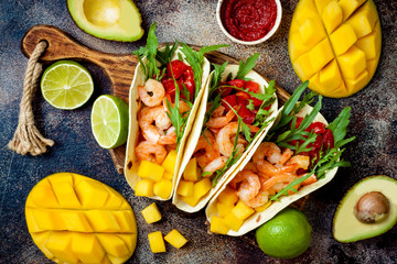 Mexican shrimp tacos with avocado, tomato, mango salsa on rustic stone table. Recipe for Cinco de...