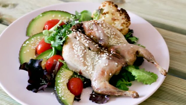 Image of quail-tobacco with sesame which served with salad of avocado and greenery on the plate indoors.
