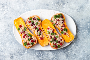 Stuffed butternut squash with chickpeas, cranberries, quinoa cooked in nutmeg, cloves, cinnamon. Thanksgiving dinner recipe. Vegan healthy seasonal fall or autumn food