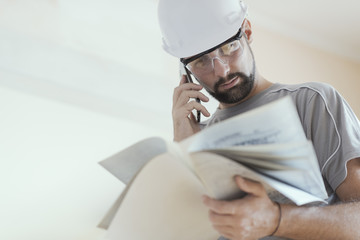 Professional construction worker checking a project and calling