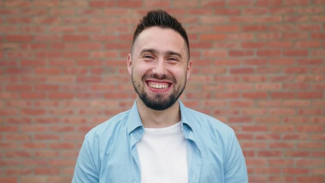 A man with a beard smiling against a brick wall background. Medium shot. Soft focus