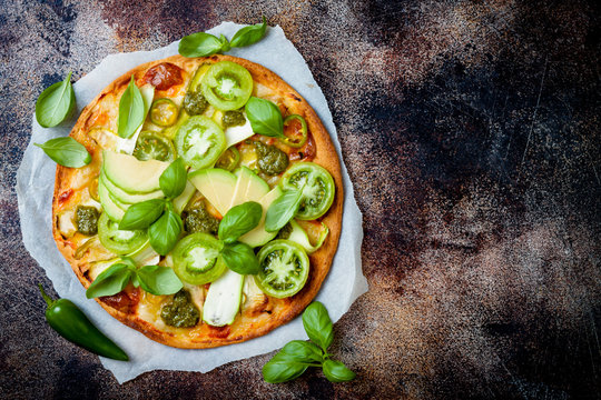 Green pizza with pesto, zucchini, tomatoes, avocado, jalapeno, mozzarella cheese and fresh basil