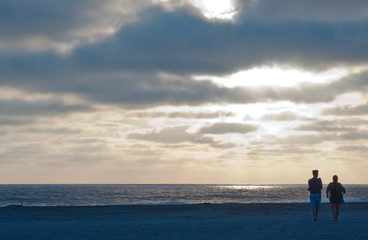 Two people walking towards the Pacific ocean on the beach in southern California, USA at sunset