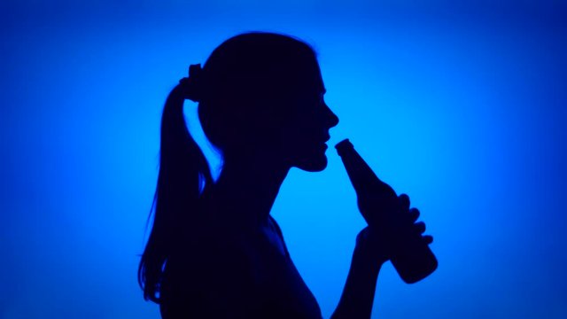 Silhouette of young woman opening can beer bottle on blue background. Female's face in profile drinking beer from glass bottle. Black contur shadow of teenager's half-face