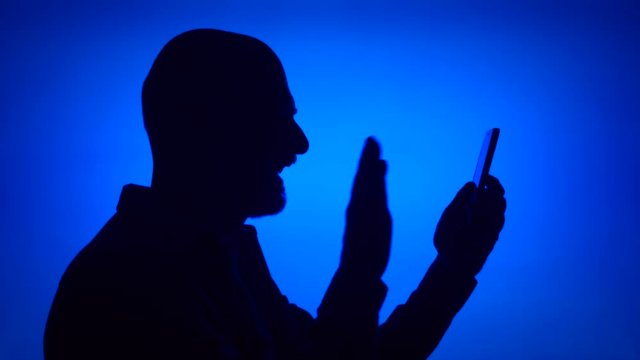 Silhouette of senior man using mobile on blue background. Male's face in profile having video chat via online app on cellphone. Black contur shadow of grandfather's half-face