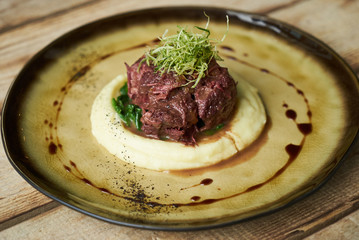 Braised beef with red wine, close-up. Jerusalem Artichoke Puree, spinach and truffle oil with baked meat in aceramic plate at restaurant table
