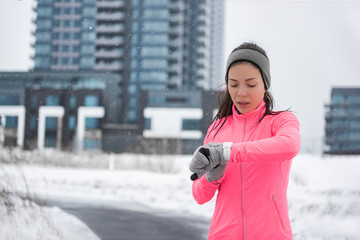 Winter running smartwatch fitness girl in cold snow weather jogging outside on street wearing smart...