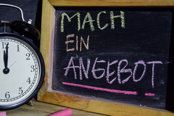 Mach ein angebot in germany on phrase colorful handwritten on blackboard. Education and business concept. Alarm clock, chalk, books on black background