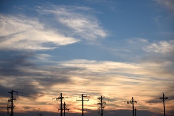 Row of utility poles and power lines, silhouette at sunset.