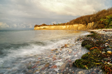 Wide beach with seaweed and stones in the evening light, overlooking the water and the steep bank, water movement in long exposure - Location: Germany, Rügen Island