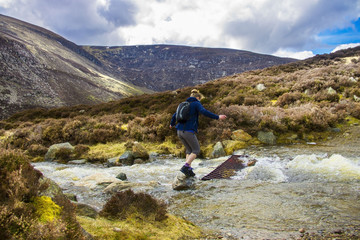 A tourist crossing the brook on the route to Mount Keen. Angus, Aberdeenshire, Scotland, UK.