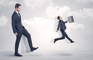 Big businessmen kicking himself as a small employee with cloudy background
