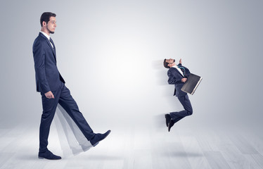 Big man in suit kicking out little himself with simple white wallpaper
