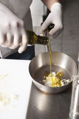 The cook pours olive oil from the bottle into the frying pan to prepare the dish in the kitchen of the restaurant, selective focusing