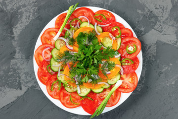 Salad of fresh vegetables on the white plate on the gray background. Top view