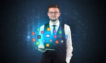 Handsome businessman in suit with tablet on his hand and application icons above
