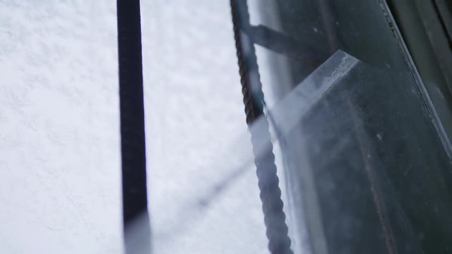Piece of broken glass sheet with sharp edges in large window having two external black vertical parallel protecting bars in day lighting.
