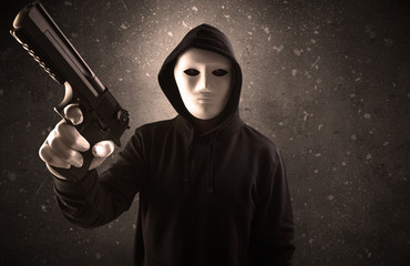Masked armed villain in empty dark room with gun ax chainsaw mallet wrench
