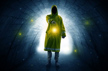 Ugly man in raincoat walking with glowing lantern in a dark tunnel