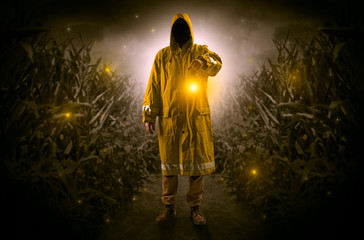 Man in raincoat at night coming from thicket and looking something with glowing lantern
