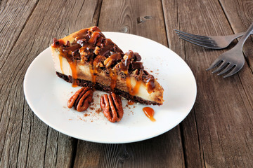 Slice of pecan caramel cheesecake with a rustic wood background. Delicious autumn dessert.