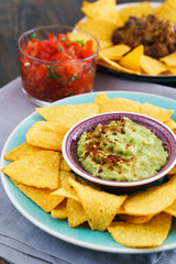 Mexican food: chili con carne, guacamole and salsa served with nachos. Dark table, high resolution.