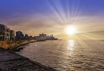 Fototapeta na wymiar Sunset over Malecon and Atlantic Ocean with residential building and visible sun rays - Havana, Cuba 