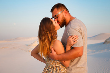 Fototapeta premium lovely attractive couple kissing on the white sand beach or in the desert or in the sand dunes, happy couple embracing at the beach on a sunny day, couple in love