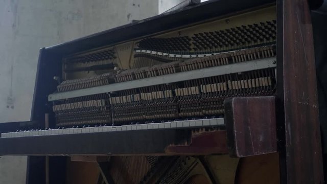 Representation of abandoned, obsolete dusty wooden piano with broken body frame and revealed inside hammers and strings in depressive large ruined room next to white walls and big windows.