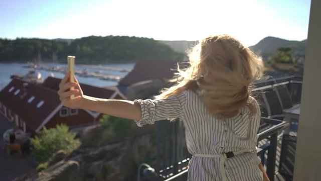 Young redhead woman taking picture of herself on the terrace on the coast in Northern Europe. Slow motion
