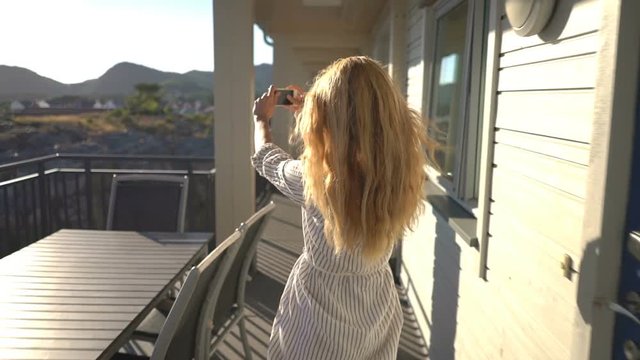 Young redhead woman taking picture on hotel terrace on the coast in Northern Europe. Slow motion