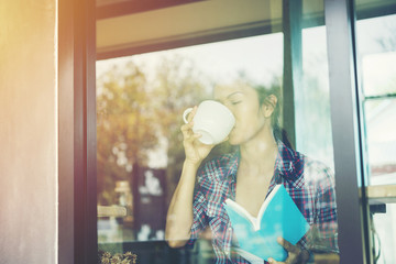 Young woman drinking coffee and reading book sitting indoor in urban cafe.