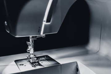 Modern compact electric sewing machine in the evening. View of needle and thread. Illumination from the built-in incandescent lamp. Sewing machine is used to stitch fabric and other materials together