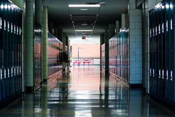 Straight view of darkly lit hallway with bright light at end and lockers covering the walls on either side 