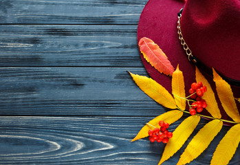 Hat burgundy color on a gray wooden background with autumn red, yellow leaves. Fashion trend...