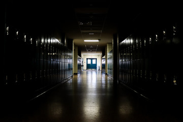 Straight view of darkly lit hallway with bright light at end and lockers covering the walls on either side 